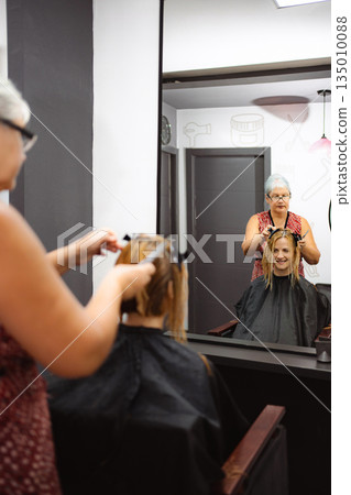 Hairdresser cutting client's hair reflecting in mirror 135010088