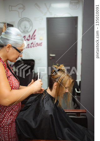Hairdresser cutting woman's wet hair in salon preparing for new style 135010091