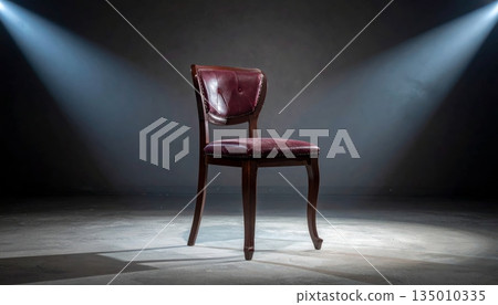 An empty vintage wooden armchair sits alone on the dark floor of an old house interior with light from a window hitting the antique furniture design in a quiet living room 135010335