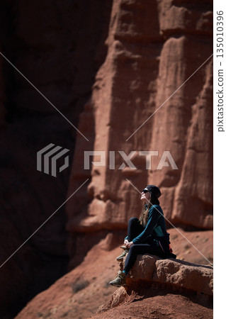 Woman traveler sits on red rock, enjoying vast landscape. Adventure travel Woman traveler sits on red rock, enjoying vast landscape. Adventure travel 135010396
