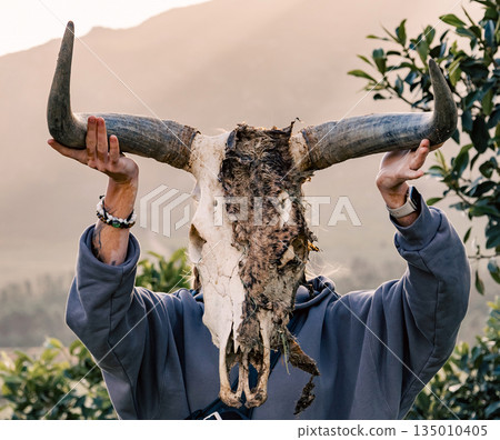 Person holding up weathered animal skull with large horns in front of their face Person holding up weathered animal skull with large horns in front of their face 135010405