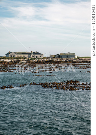 Distant view of small settlement on rocky island from ocean. Coastal landscape Distant view of small settlement on rocky island from ocean. Coastal landscape 135010435