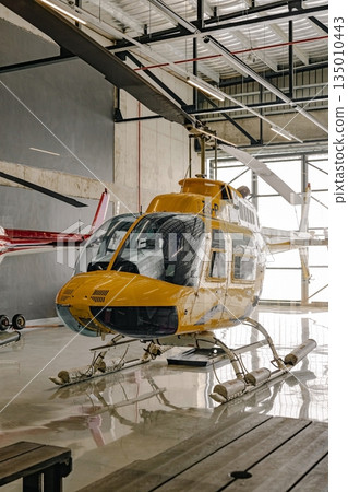 Yellow helicopter parked inside a hangar with propeller blades Yellow helicopter parked inside a hangar with propeller blades 135010443