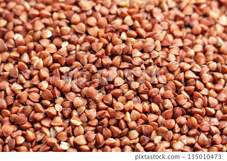 Brown grains of uncooked buckwheat groats close up. Healthy food ingredient Brown grains of uncooked buckwheat groats close up. Healthy food ingredient 135010473