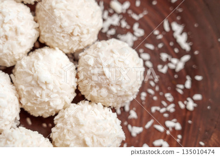 Soft spherical sweets coated in coconut flakes on a dark wooden surface Soft spherical sweets coated in coconut flakes on a dark wooden surface 135010474
