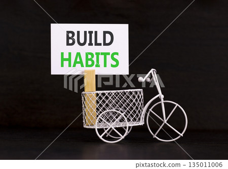 Build habits symbol. Concept word Build habits on beautiful white paper. Beautiful wooden clothespin. Miniature black bicycle. Beautiful orange background. Business build habits concept. Copy space. Build habits symbol. Concept word Build habits on beautiful white paper. Beautiful wooden clothespin. Miniature black bicycle. Beautiful orange background. Business build habits concept. Copy space. 135011006