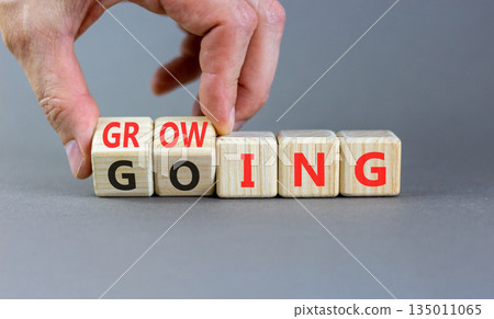 Going and growing symbol. Concept words Going Growing on beautiful wooden blocks. Beautiful grey background. Businessman's hand. Business going and growing concept. Copy space. Going and growing symbol. Concept words Going Growing on beautiful wooden blocks. Beautiful grey background. Businessman's hand. Business going and growing concept. Copy space. 135011065