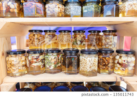 Jars of honey with various nut fillings stand on the shelf. Honey products. Jars of honey with various nut fillings stand on the shelf. Honey products. 135011743