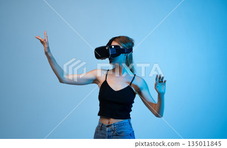 Side view of young woman using VR headset and controlling virtual interface with hand gestures, immersive technology and future digital concept Side view of young woman using VR headset and controlling virtual interface with hand gestures, immersive technology and future digital concept 135011845