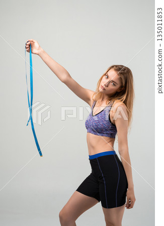 Fit young woman holding measuring tape, fitness progress, body measurement and healthy active lifestyle concept 135011853