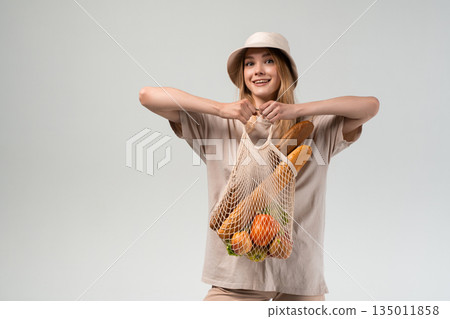 Young woman holding reusable mesh shopping bag with fresh groceries and bread, sustainable food shopping, eco friendly lifestyle and healthy everyday choices Young woman holding reusable mesh shopping bag with fresh groceries and bread, sustainable food shopping, eco friendly lifestyle and healthy everyday choices 135011858
