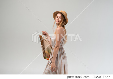 Attractive young woman carrying reusable mesh bag with groceries over shoulder, healthy food shopping concept, eco friendly lifestyle, conscious consumer behavior Attractive young woman carrying reusable mesh bag with groceries over shoulder, healthy food shopping concept, eco friendly lifestyle, conscious consumer behavior 135011866