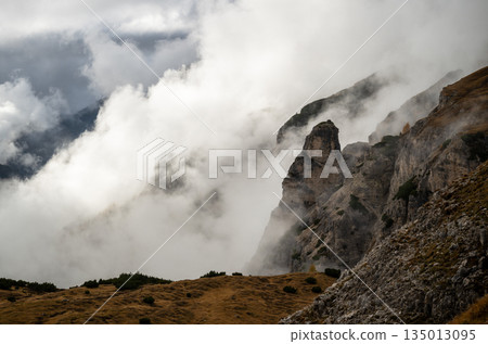 Fog rolling over rugged Dolomites mountains and rocky alpine slopes 135013095