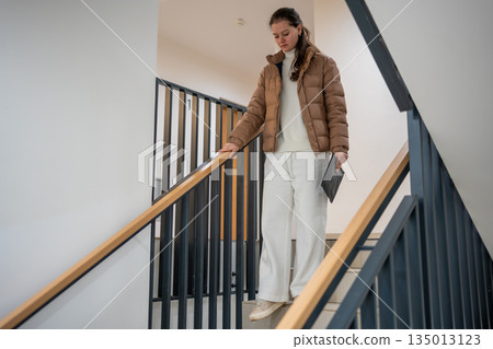 Woman walking down stairs inside apartment building. Daily movement in residential interior. 135013123