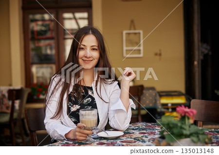 holding cup coffee, Holding Cup, Relaxed Atmosphere. Young woman smiles while holding coffee cup at charming outdoor cafe, creating welcoming and relaxed atmosphere. 135013148