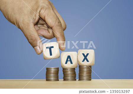 Tax Concept with Hand Placing Wooden Blocks on Stacks of Coins, Hand placing wooden blocks with the word TAX on stacks of coins, symbolizing finance, taxation, economic policy, 135013297