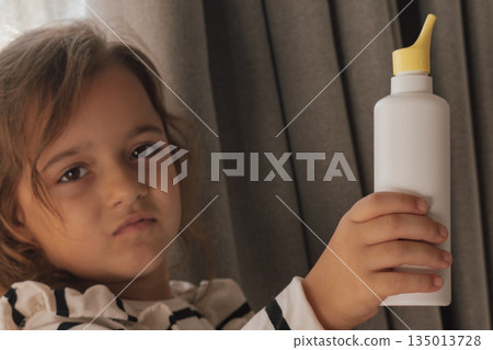 Cute girl holding an unbranded saline nasal spray bottle for children's health care Cute girl holding an unbranded saline nasal spray bottle for children's health care 135013728