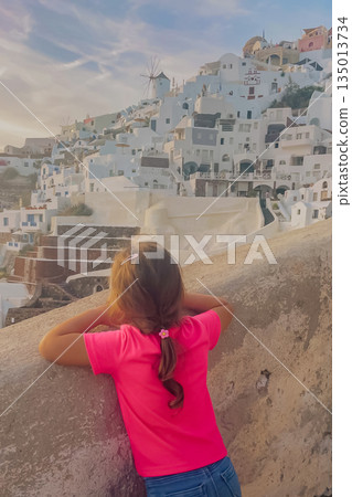Joyful moment: a young figure enjoying the sunny day and the stunning caldera views on the beautiful island of Santorini. Joyful moment: a young figure enjoying the sunny day and the stunning caldera views on the beautiful island of Santorini. 135013734
