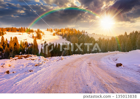 winter landscape with snow covered country road winding through fir forest in mountains at sunset. alpine countryside of in evening light. timeless nostalgia book cover with rainbow winter landscape with snow covered country road winding through fir forest in mountains at sunset. alpine countryside of in evening light. timeless nostalgia book cover with rainbow 135013838