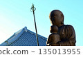 Jizo Bodhisattva statue with blue sky and temple tile roof in the background 135013955