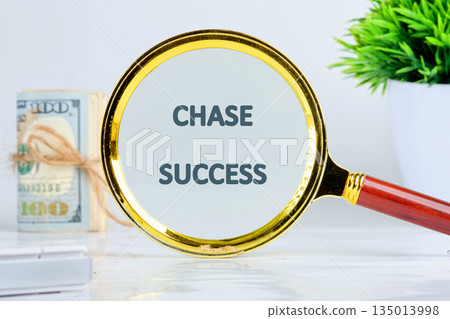A magnifying glass focuses on the words CHASE SUCCESS. A stack of money is tied together with string, suggesting financial aims, while a potted plant symbolizes growth and prosperity A magnifying glass focuses on the words CHASE SUCCESS. A stack of money is tied together with string, suggesting financial aims, while a potted plant symbolizes growth and prosperity 135013998