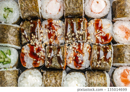 Assorted sushi rolls with eel sauce sesame and seafood top view Assorted sushi rolls with eel sauce sesame and seafood top view 135014699