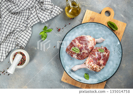 Raw duck legs with spices, basil, and olive oil on ceramic plate, top view, free space for text 135014758