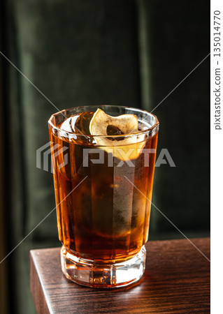 Whiskey cocktail with ice and dried fruit garnish in crystal glass on dark background, close up Whiskey cocktail with ice and dried fruit garnish in crystal glass on dark background, close up 135014770