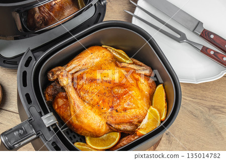 Whole roasted chicken with orange slices in air fryer on wooden table, top view, free space for text 135014782
