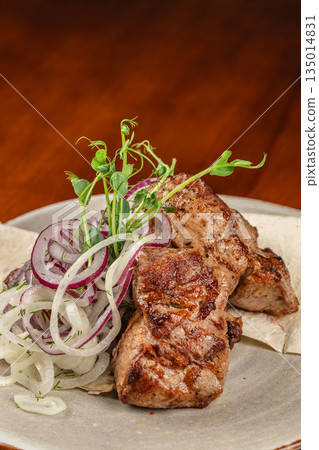 Grilled meat with fresh onion rings and herbs on a plate Grilled meat with fresh onion rings and herbs on a plate 135014831
