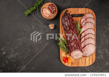 Smoked meat slices with spices and herbs on a wooden cutting board with copy space on dark background Smoked meat slices with spices and herbs on a wooden cutting board with copy space on dark background 135014851