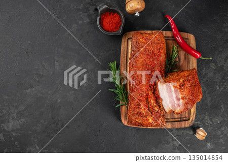 Spicy smoked pork loin with chili peppers and herbs on a wooden cutting board with copy space on dark background Spicy smoked pork loin with chili peppers and herbs on a wooden cutting board with copy space on dark background 135014854
