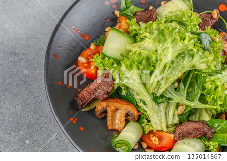 Fresh salad with grilled beef, lettuce, mushrooms, cucumbers, and tomatoes on a black plate with copy space Fresh salad with grilled beef, lettuce, mushrooms, cucumbers, and tomatoes on a black plate with copy space 135014867