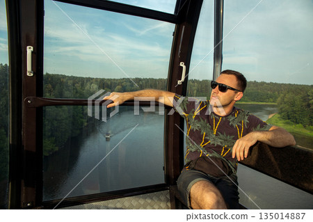 Man enjoying aerial view from a cable car over a scenic river Man enjoying aerial view from a cable car over a scenic river 135014887