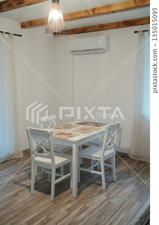 Minimalist dining area with white wooden table and chairs in a bright apartment interior. Clean composition reflects simplicity comfort and everyday home lifestyle 135015095