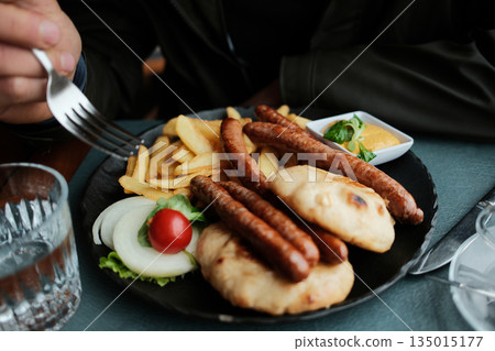 Grilled sausages with fries, flatbread and sauce served in a cafe. The image shows casual dining and Balkan comfort food concept 135015177