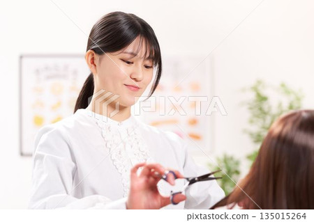 Young female hairdresser cutting a customer's hair 135015264
