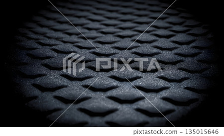 Black textured diamond grid surface with deep embossed geometric pattern on matte industrial material in dramatic shadow closeup view. AI Generated 135015646