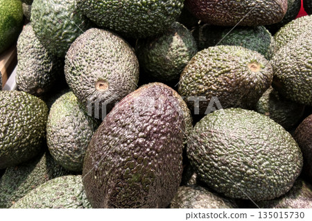Avocados are arranged in a market display, showcasing their natural texture. The scene captures shoppers browsing for fresh produce in the afternoon Avocados are arranged in a market display, showcasing their natural texture. The scene captures shoppers browsing for fresh produce in the afternoon 135015730