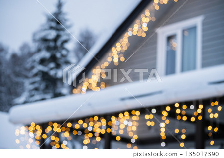 Snowy blurred winter house in forest with bokeh of festive Christmas lights on creating dreamy holiday atmosphere and warm seasonal background. Celebration themes. Snowy blurred winter house in forest with bokeh of festive Christmas lights on creating dreamy holiday atmosphere and warm seasonal background. Celebration themes. 135017390