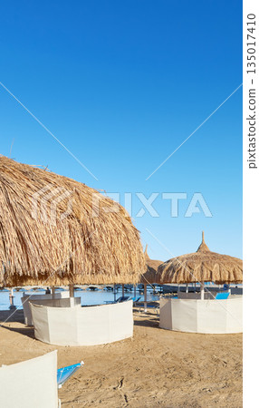 Straw umbrellas, sun loungers and windbreaks on the beach in Hurghada, Egypt. Straw umbrellas, sun loungers and windbreaks on the beach in Hurghada, Egypt. 135017410