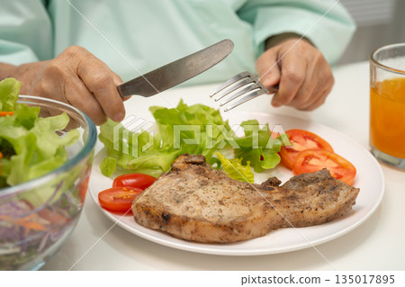 Asian elderly woman patient eating pork chop stake and vegetable salad for healthy food in hospital. Asian elderly woman patient eating pork chop stake and vegetable salad for healthy food in hospital. 135017895