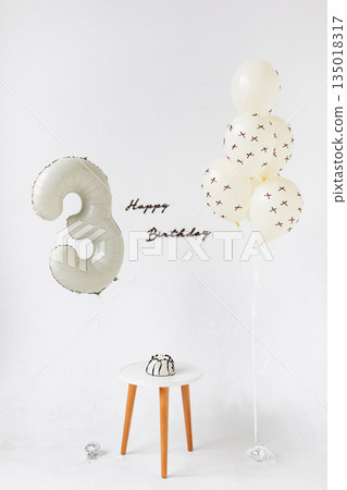 A minimalist birthday scene featuring a number three balloon, balloons, a small cake, and a 'Happy Birthday' message against a white backdrop. A minimalist birthday scene featuring a number three balloon, balloons, a small cake, and a 'Happy Birthday' message against a white backdrop. 135018317