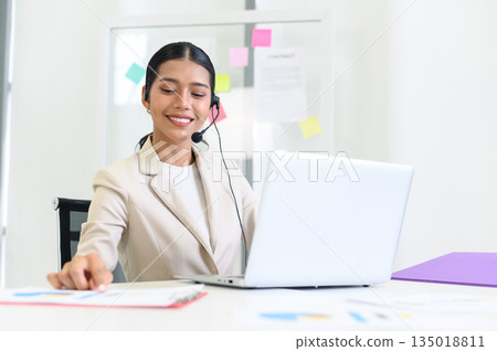 Young beautiful friendly operator woman with headset working in a call center. customer service pay attention and talking to customers while using computer at office. Young beautiful friendly operator woman with headset working in a call center. customer service pay attention and talking to customers while using computer at office. 135018811