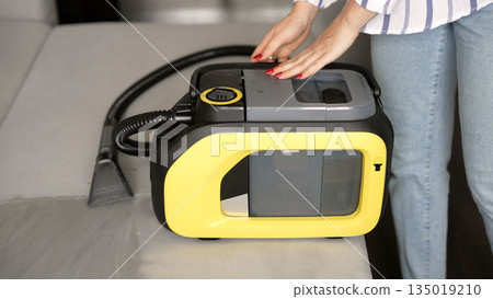 Woman preparing a convertible sofa for cleaning with an upholstery extractor Woman preparing a convertible sofa for cleaning with an upholstery extractor 135019210