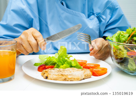 Asian elderly woman patient eating salmon stake and vegetable salad for healthy food in hospital. 135019619