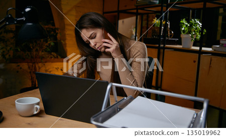 Tired woman multitasking with phone and laptop at work. Tired woman multitasking with phone and laptop at work. 135019962