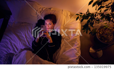 Woman using smartphone in bed at night with screen light. Woman using smartphone in bed at night with screen light. 135019975