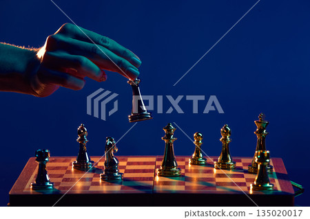 Hand hovering chess piece above opposing pieces. Hand hovering chess piece above opposing pieces. 135020017