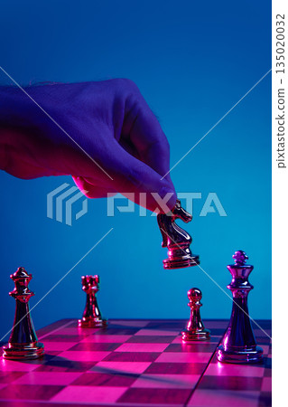 Hand holding chess knight above game board in neon. Hand holding chess knight above game board in neon. 135020032